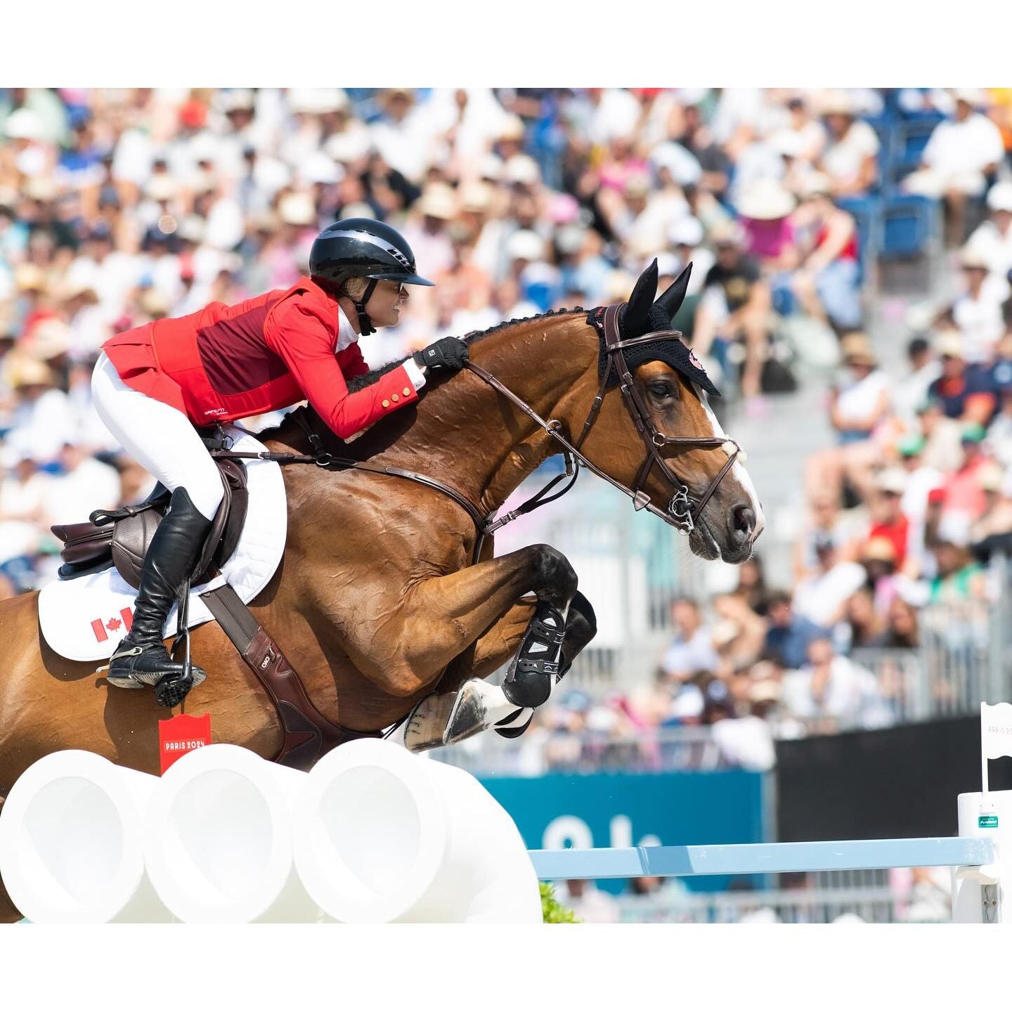 Canadian show jumper Erynn Ballard competing in a red SAFEFIT airbag vest, jumping a white obstacle at the Paris Olympics.